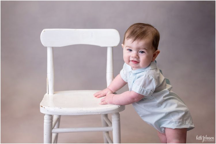 baby boy in vintage romper pulling up on chair
