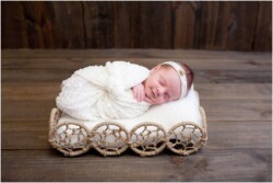 smiling newborn in white wrap on wood floor