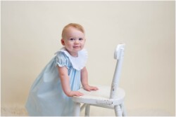 baby girl in blue dress holding chair