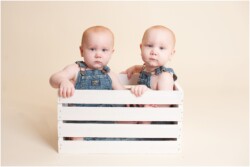 twin boys in overalls sitting in white crate