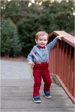 one year old in suspenders outside on bridge