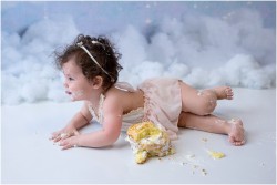 baby girl laying down next to her smash cake