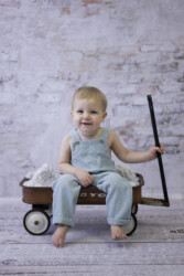 baby sitting in wagon in front of white bricks